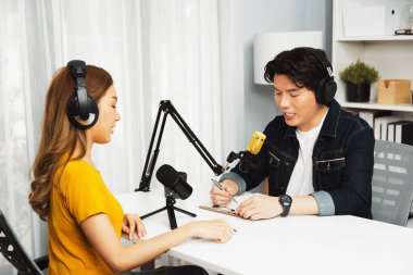 Gülümseyen radyo etkili sunucusu kulaklık takıyor kadın konuşmacı ile röportaj yapıyor sosyal medya internet sitesinden dinleyicilere bilgi paylaşıyor stüdyo kaydında sabah canlı yayın kanalı. İnfobahn.