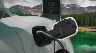 Temiz çevre için temiz enerjinin yol açtığı ilerici elektrikli araba kavramının arka planı olarak dağın tepesinde bulutun zaman kavramının yer aldığı doğal manzara. EV araba şarj istasyonunda şarj oluyor..
