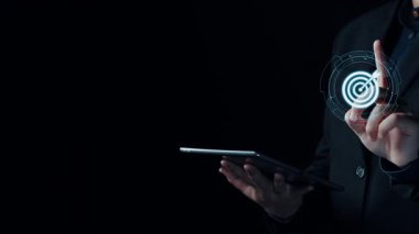 Hedef grafik ve analitik sembollerin yer aldığı dijital pazarlama stratejisini sergileyen bir profesyonel. Bu görüntü, modern iş stratejilerinde veri görselleştirmesinin önemini vurgular. Dörtgen