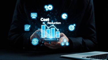 Bir iş adamı akıllı telefonunda dijital grafikler ve simgelerle ilgilenerek çeşitli maliyet azaltma stratejileri sergiliyor. Karanlık zemin modern teknolojiyi ön plana çıkarıyor. Dörtgen