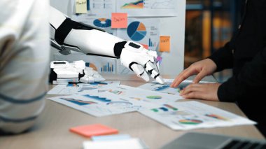 Bir robot kol, üretkenliği artırmak için renkli grafikler ve raporlar yoluyla sunulan iş ölçümlerini ve verileri analiz ederek bir ofis ortamında bir insanla işbirliği yapar.