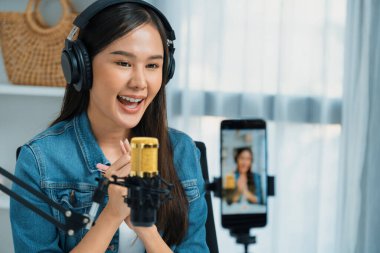 Asyalı sunucu canlı yayında canlı yayında canlı yayında sosyal medyada kulaklık takarak konuşuyor. Dinleyicileri modern stüdyoda koçluk yaparak selamlıyor. Taktik.