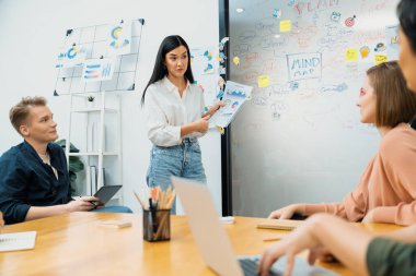 Güzel, genç, beyaz bir lider, modern iş toplantı odasındaki belgeye işaret ederken, profesyonel yatırımcılara grafik ve zihin haritası kullanarak yaratıcı pazarlama stratejisi sunuyor. Tertemiz..