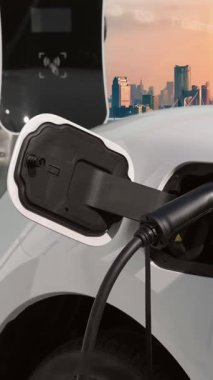 Elektrikli araç, EV araba şehir merkezindeki şarj istasyonunda şarj oluyor. Etrafı yüksek gökdelenlerle çevrili. Çevre dostu yenilikçi temiz enerji kavramı.