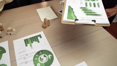 Şirketin gelecekteki EG 'si için yeşil enerji grafiği kullanımına danışmanlık ve analiz yapan iş ekibi. Yel değirmeni modeli, masadaki temiz enerji ve ev bloğu sembolize edilmiş eko evi kullanarak temsil ediliyor. Tanımlama.