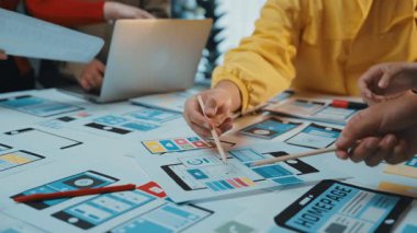 Dinamik bir ekip, teknoloji araçlarıyla dolu modern bir ofis masasında kablolar ve prototipler kullanarak mobil bir uygulama tasarlamak için ortak bir oturum başlatır. SACTR