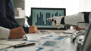 Bir robot el, işbirlikçi ekip toplantısı sırasında iş haritalarına doğru hareket eder, veri analizlerinde teknoloji ve insan çabalarının karışımını vurgular. Noogenesis