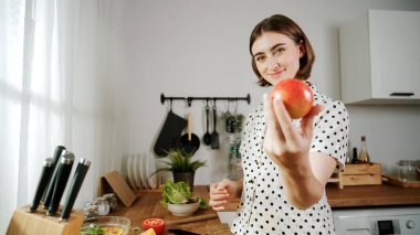 Enerjik anne sağlıklı yemek yapmak ve taze elmayı tutarken kameraya bakmak için meyve seçer. Mutlu ev bakıcısı mutfakta salata hazırlarken yemek pişirmekten zevk alır. Pedagoji.