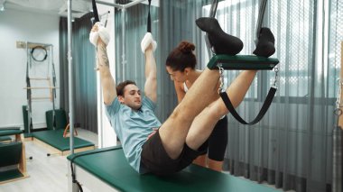 Eğitmen rehberliğinde Pilates Cadillac 'ta ters bacak yükseltme pratiği yapan sağlıklı bir müşteri. Çekirdek dayanıklılığını ve üst vücut dengesini arttırmak için Cadillac 'ı geren adam. Alışkanlık.