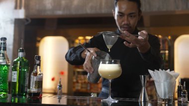 Asyalı barmen, alkollü likör ve şuruplu kokteyl bardağına kattığı her şeyi süzgeçle temizliyor. Lüks gece kulübünde gece hayatı karışımı sergileniyor. Vinosity.