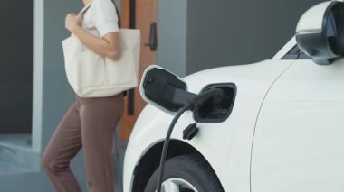 Bir kadın evinde elektrikli araç şarj aletinin fişini çekiyor. İlerici bir yaşam tarzında elektrikli araçların kullanımı, temiz ve sağlıklı bir çevreye katkıda bulunur..