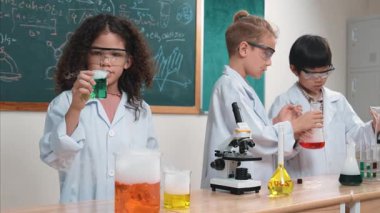 Çocuklar laboratuvarda karatahta başında dururken fen dersinde deney yapıyorlar. Mutlu öğrenci biyokimyasal sıvıyı keşfederken ve incelerken ve karıştırırken. Pedagoji.