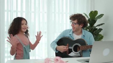 Çekici beyaz bir baba gitar çalarken tatlı bir kız müzik eşliğinde dans ediyor. Mutlu baba ve Amerikalı kız birlikte vakit geçirirken akıllı çocuk müzik yapıyor. Aile eğlence konsepti. Pedagoji.