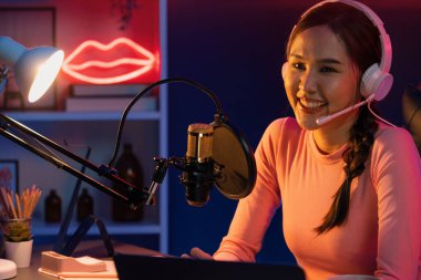 Geceleri podcast 'te olumlu konuşmalar yapan, pembe neon ışıklı modern stüdyoda sunum için dizüstü bilgisayar kullanan, gülümseyen, genç, güzel Asyalı bir etkileyiciydi. Taktik.