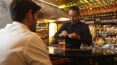 Barmen portakal kabuğu sıkar, cam kokteyl viskisinin üzerinden kokar, buz kalıbının tepesine eski moda kokar. Kulüpteki lüks gişe barında VIP müşteriye özel sunum yapar. Vinosity.