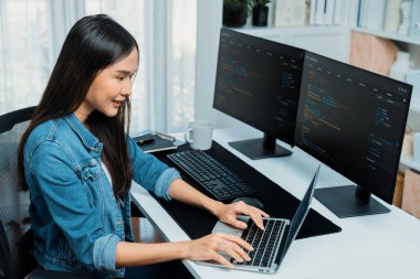 IT geliştiricisinde gülümseyen genç Asyalı dizüstü bilgisayarında kodlama programı verileriyle kotlu tişört giyerek çevrimiçi bilgi yazıyor. Güvenlik analizi iki ekran ile çevrili. Taktik.