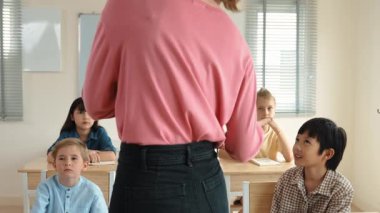 Sınıfta sınıf çalışmalarını anlatırken, sınıfta dolaşan beyaz bir öğretmen. Çekim eğitmeni konuşuyor ve çeşitli öğrenciler çalışırken ya da not alırken dersini anlatıyor. Eğitim. Pedagoji.