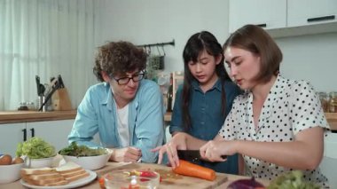 Çekici beyaz anne ve baba Asyalı kızıyla taze yemek pişirmek için birlikte vakit geçiriyorlar. Enerjik anne ve baba mutfakta salata yapmak için taze sebze hazırlıyor. Sağlıklı yiyecekler. Pedagoji.