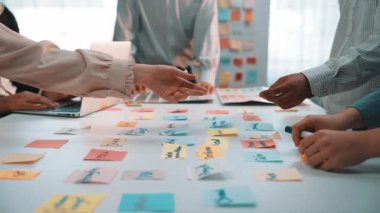 Çeşitli profesyonellerden oluşan bir grup, yenilikçi fikirler ve stratejiler üretmek için beyin fırtınası sırasında aktif olarak yapışkan notlar kullanarak modern bir ofis alanında işbirliği yapıyor. SACTR