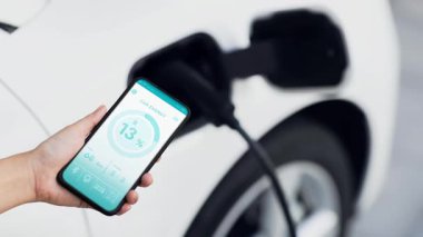 Akıllı telefon ekranı akıllı EV mobil uygulama üzerinde pil durumu EV araba garajdaki ev şarj istasyonu ile elektrik şarj ederken. Geleceğin yenilikçi EV arabası ve enerji sürdürülebilirliği. İnceleyin