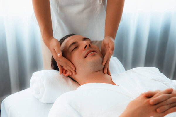Кавказский мужчина наслаждается расслабляющим анти-стрессовым массажем головы и расслабляющим отдыхом кожи лица в дневном спа современном светлом окружении на роскошном курорте или в спа-салоне отеля. Quiescent