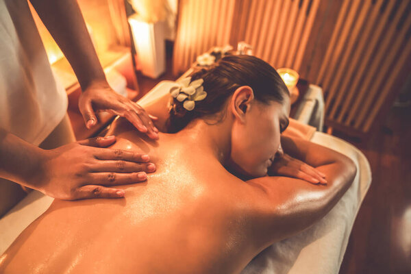 Caucasian woman customer enjoying relaxing anti-stress spa massage and pampering with beauty skin recreation leisure in warm candle lighting ambient salon spa at luxury resort or hotel. Quiescent