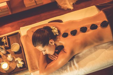 Lüks tatil köyündeki kaplıcalarda sıcak taş masajı, sıcak mum ışığı, spa bazalt taşı masajının keyfini çıkaran mutlu kadın müşteriler, rahatlatıcı bir sıcaklıkla vücudun üzerinde süzülüyorlar. Sessiz.