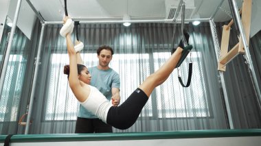 Pilates eğitmeni, Cadillac teçhizatı üzerinde asılı duran bir bacak egzersizinde bir müşteriye rehberlik ediyor. Vücut dengesini sağlamak için Cadillac 'ı geren sağlıklı bir kadın. Alışkanlık.