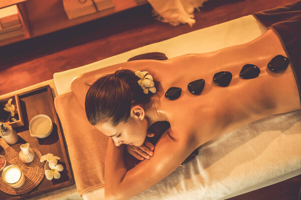 Массаж горячими камнями в спа-салоне на роскошном курорте с теплым свечой, блаженная женщина-клиент наслаждаясь спа-массаж базальтового камня скользить по телу с успокаивающим теплом. Quiescent