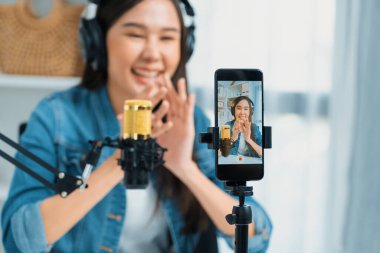 Asyalı sunucu canlı yayında canlı yayında canlı yayında sosyal medyada kulaklık takarak konuşuyor. Dinleyicileri modern stüdyoda koçluk yaparak selamlıyor. Taktik.