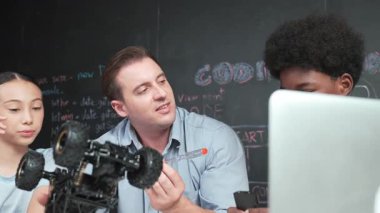 Akıllı öğretmen araba modelini farklı öğrencilere denetliyor. Melez ırk dinleyen liseli çocuklar masada dizüstü bilgisayarı ve kabloları olan robot model sistemini açıklıyor. Öğretim