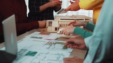 Mimarlar ve tasarımcılardan oluşan dinamik bir grup, ayrıntılı ölçekli bir model ve renkli planlar incelerken inşa planlarını tartışarak yaratıcı bir oturuma girişiyor. SACTR