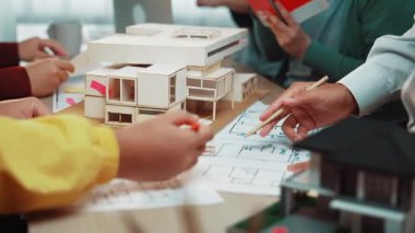 Tasarım toplantısına katılan mimarların elleri mevcut taslaklar ve model bir yapı, modern bir çalışma alanında yenilikçi çözümleri teşvik eden takım çalışması ve yaratıcılık sergiliyor. SACTR