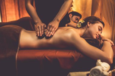 Sıcak mum ışığı olan lüks bir tatil köyündeki kaplıca salonunda sıcak taş masajı yapan mutlu çift, bazalt taşı masajının keyfini çıkarırken rahatlatıcı bir sıcaklıkla vücudun üzerinde süzülüyor. Sessiz.