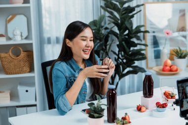 Gülümseyen, güzel Asyalı genç, lezzetli karışık çilek ve kiraz suyu detoksu içeceklerini inceleyen, sosyal medyada özel promosyon satışı için sağlıklı ürünler sergileyen. Taktik.