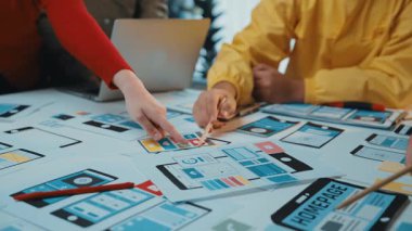 Çeşitli bir ekip, modern ofis ortamında mobil bir uygulama için kablolar ve prototipler üzerinde odaklanarak, bir kullanıcı arayüzü tasarım oturumu sırasında işbirliği yapar. SACTR