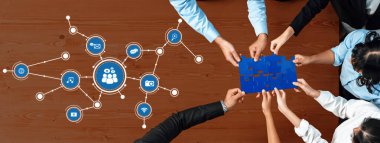 Dinamik bir ekip, ahşap bir masa üzerinde, iletişimi ve yenilikçi düşünceyi vurgulayarak, bulmaca parçaları ve teknoloji simgeleri kullanarak işbirlikçi problem çözme işine girişiyor. Dostluk