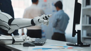 Bir robotik el klavyenin üzerinde teknolojinin ve insan etkileşiminin üretkenlik ve yenilik odaklı çağdaş ofis ortamındaki karışımını gösteren jestler yapar. Noogenesis