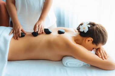 Lüks tatil köyündeki kaplıcalarda sıcak taş masajı. Gün ışığı sükunet ortamında, mutlu kadın müşteri bazalt taş masajından zevk alıyor. Rahatlatıcı bir sıcaklıkla vücudun üzerinde süzülüyor. Sessiz.