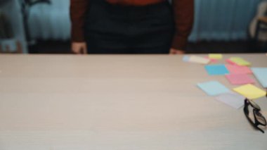 Kırmızı kazak giyen bir kişi çalışma masasının üzerinde renkli yapışkan notlar ve gözlüklerle süslenerek yaratıcılık ve planlama için davetkar bir ortam yaratıyor. SACTR