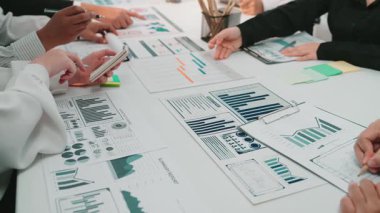 Modern bir ofiste işbirliği içinde çalışan bir iş adamı grafikleri ve grafikleri analiz eder. Görüşmede performansı artırmak ve hedeflere ulaşmak için stratejiler ve içgörüler ele alınıyor. SACTR