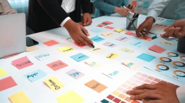 Değişik bir beyin fırtınası yapan ve yaratıcı fikirler üretmek için renkli yapışkan notlar ve dizüstü bilgisayarlar kullanan farklı bir ekibi gösteren canlı ve dinamik bir ofis sahnesi. SACTR