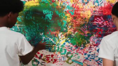 Genç ve çeşitli çocukların arka görünüşleri renkli duvarları elle boyarlar. Çekici bir lise öğrencisi renk paletini tutarken duvarı el iziyle boyuyor. Yaratıcı aktivite. Öğretim