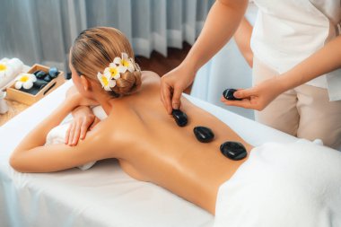 Lüks tatil köyündeki kaplıcalarda sıcak taş masajı. Gün ışığı sükunet ortamında, mutlu kadın müşteri bazalt taş masajından zevk alıyor. Rahatlatıcı bir sıcaklıkla vücudun üzerinde süzülüyor. Sessiz.