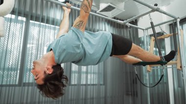Çekirdek dayanıklılığı ve spor salonunda vücut egzersizi için pilates trapez masasına tırmanan bir adam. Eğitmen, arka ve kalça esnekliğini arttırmak için Cadillac 'ta ters asılı duruyor. Alışkanlık.