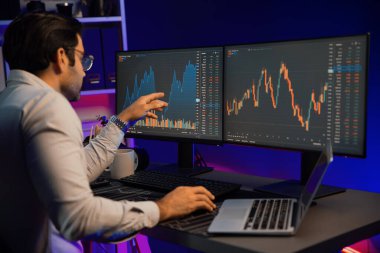 Akıllı tüccar işadamı, karanlık oda gecesinde neon ışıklı ofisteki arama pazarında yüksek kârla ekranda bilgisayar ve bilgisayar üzerinde dinamik borsa yatırımları üzerinde yoğunlaşıyor. Tahmin et..