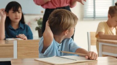 Kafkasyalı zeki çocuk, ilkokulda öğretmenlerin geçişi sırasında sınıfta okuyan çeşitli çocuklarla çevrili öğretmenlere sorduğu ve cevap verdiği için elini kaldırıyor. Eğitim konsepti. Pedagoji.