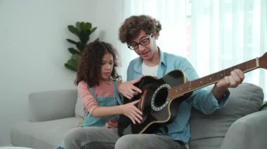 Beyaz bir baba, tatlı kızına koltukta otururken gitar çalmayı öğretiyor. Müzik öğrenirken babasına gitar çalarken bakan tatlı öğrenci kız. Aile eğlence konsepti. Pedagoji.