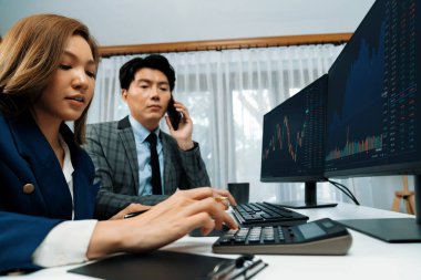 Gülümseyen Asyalı işadamı komisyoncu dinamik borsa veritabanını arıyor. Kadın iş ortağı, iç işyerindeki kar eden uygulama programını karşılaştıran ekranlara işaret ediyor. İnfobahn.