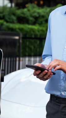 Modern iş adamı akıllı telefonun 3D hologramından batarya durumunu kontrol ederken EV arabasının şarj olan enerjisini kontrol ediyor. Gelecekteki EV otomotiv teknolojisinin yenilikçi teknolojik gelişimi. İnceleyin